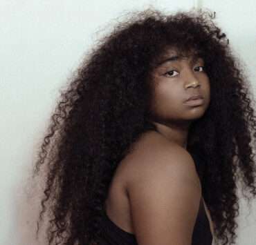 Confident Black woman with long natural curly hair looking over shoulder, expressing bold self-identity and style