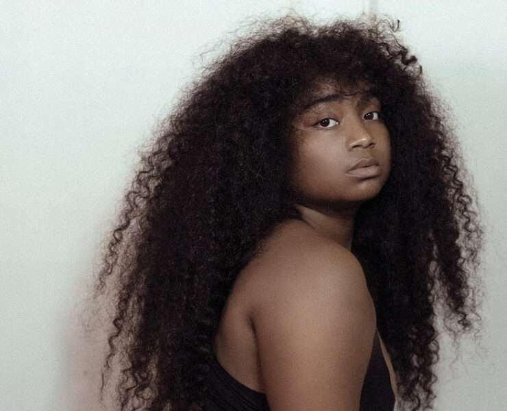 Confident Black woman with long natural curly hair looking over shoulder, expressing bold self-identity and style