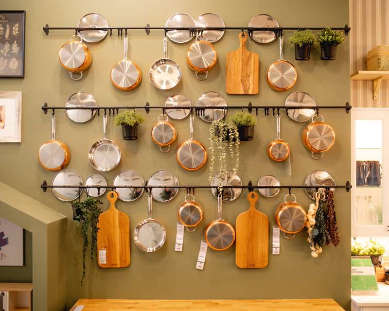 IKEA House Warming IKEA Union Square kitchen display wall featuring copper cookware, cutting boards, and hanging plants arranged in a stylish Scandinavian design.
